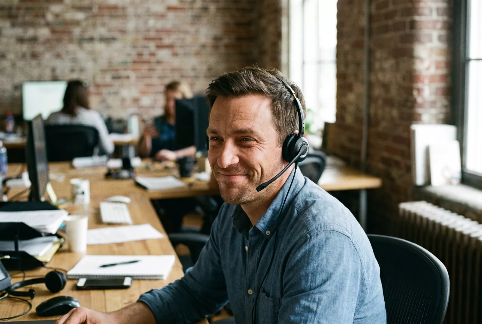 Recruitment consultant on a headset at his desk in a busy agency office