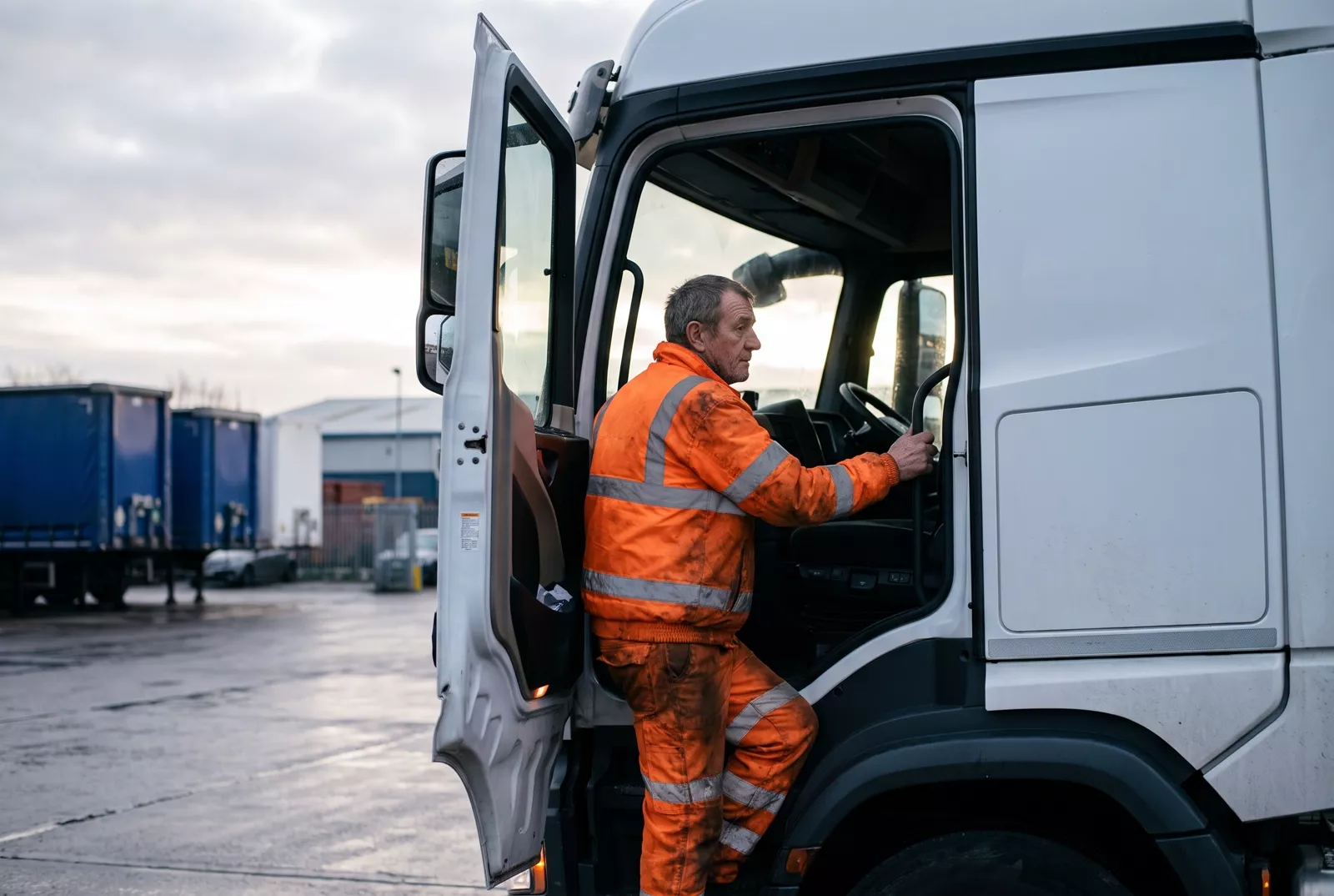 HGV driver climbing into the cab of an articulated lorry at a depot
