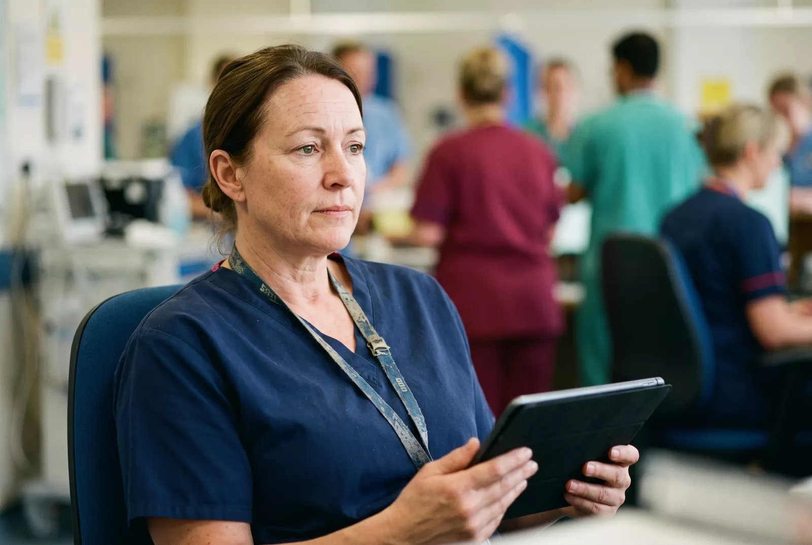 NHS nurse reviewing a tablet at a ward nurses' station